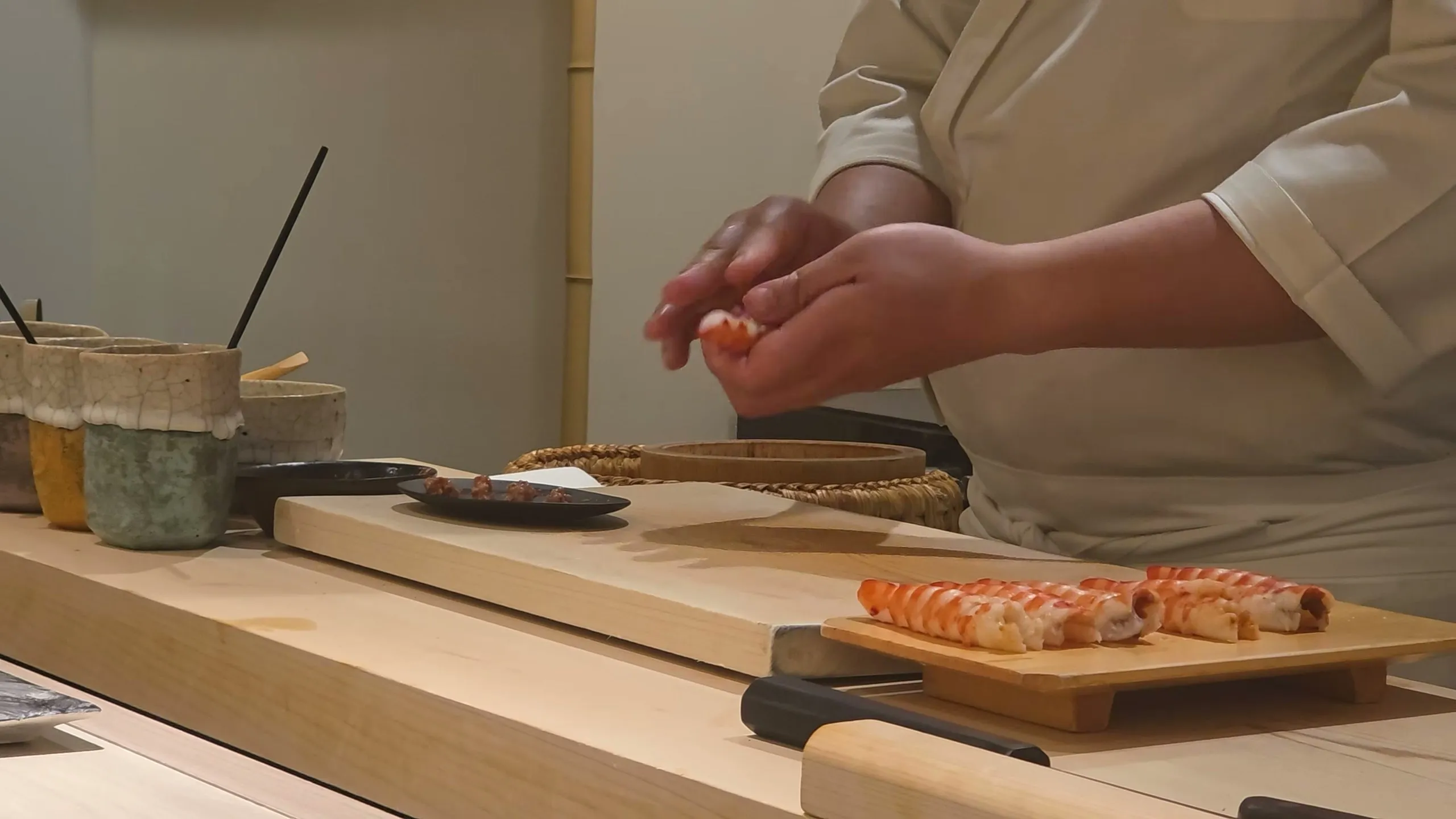 A chef shaping kuruma prawn nigiri with cooked prawns lined up on a wooden board