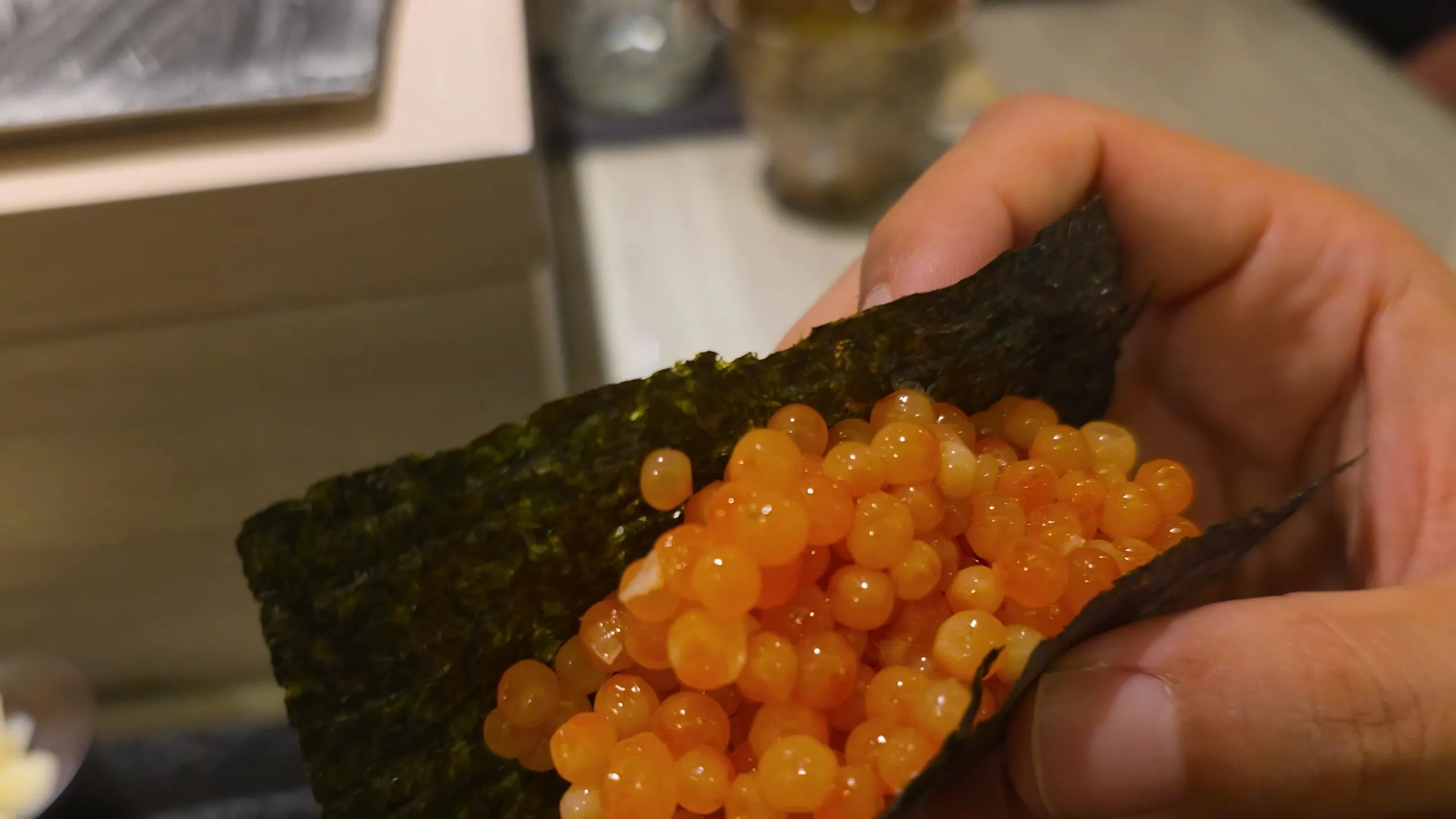Ikura hand roll held over the Shimazu counter