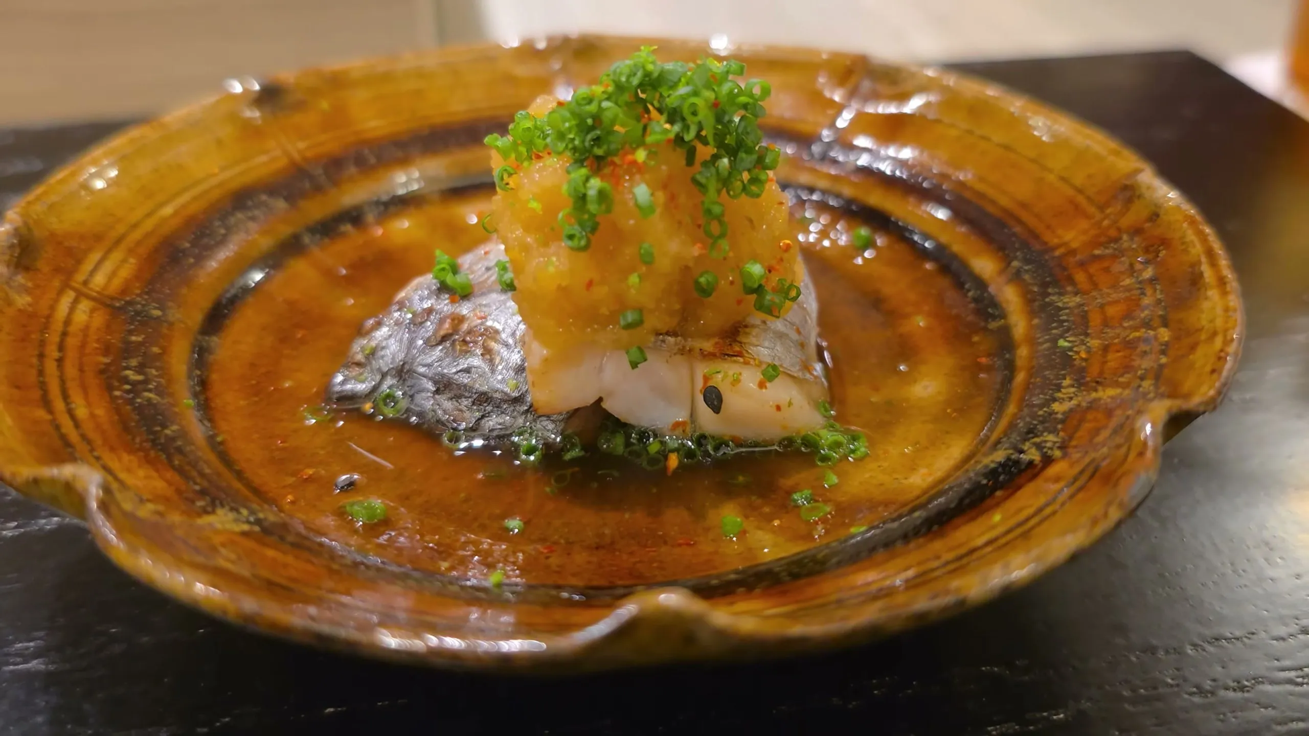 Grilled cutlassfish topped with grated daikon and chives on an amber plate